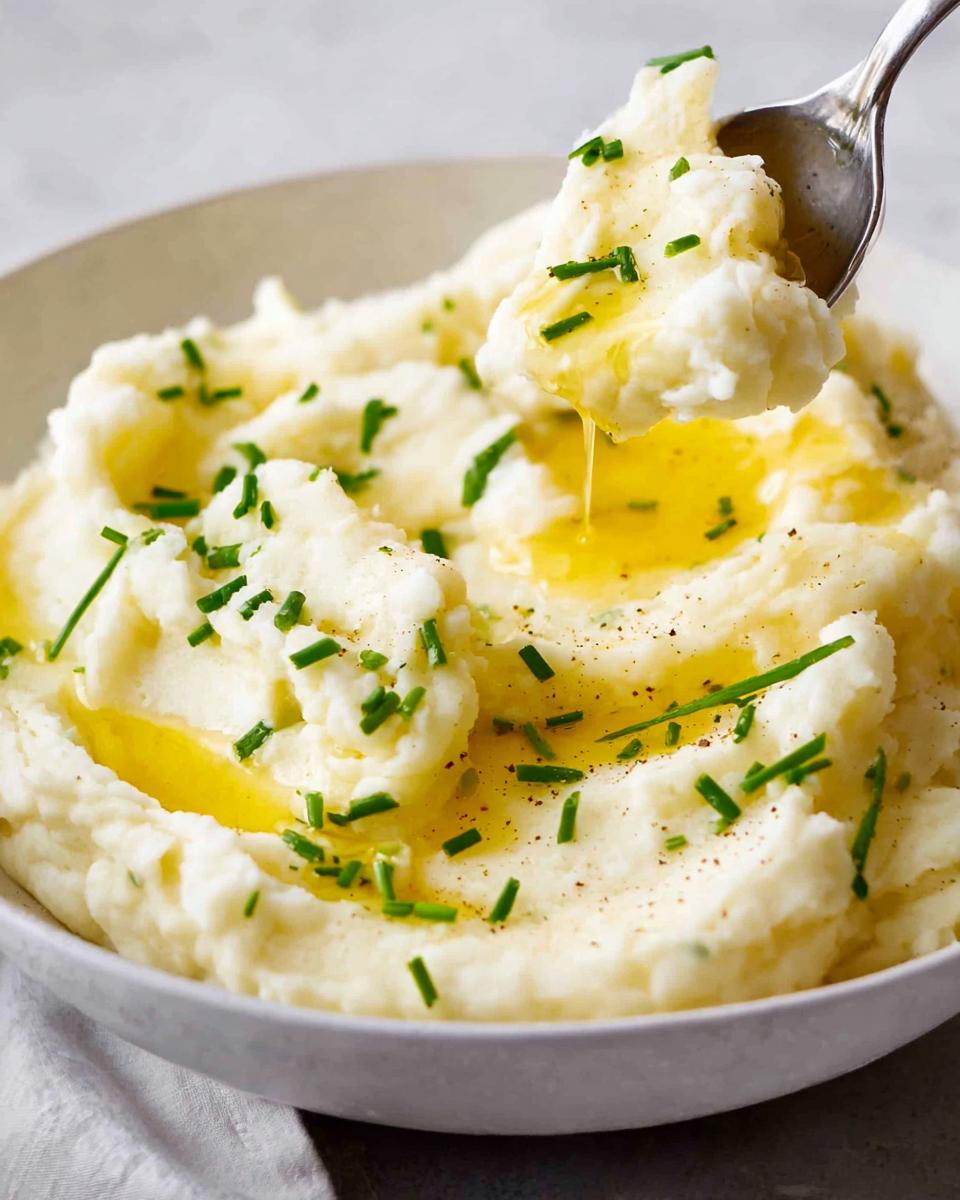 A spoonful of creamy 12-Ingredient Mashed Potatoes topped with melted butter and fresh chives.