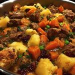 Close-up of a hearty beef stew with chunks of beef, potatoes, carrots, peas, cranberries, and croutons in a pot.