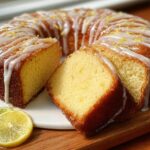 A sliced 7UP cake with a lemon glaze and zest, garnished with lemon and lime slices.