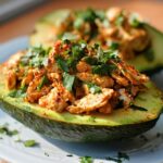 Two halves of an avocado filled with seasoned shredded chicken and fresh cilantro, part of quick sandwich ideas.