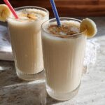 Two tall glasses of creamy banana peanut butter smoothie, topped with peanut butter drizzle and garnished with banana slices. A great breakfast idea.