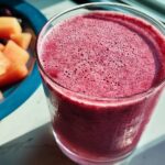 A vibrant berry smoothie in a glass, with a side of diced melon and blueberries, perfect for breakfast ideas.