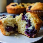 A blueberry muffin, split in half, revealing a fluffy interior packed with juicy blueberries. Part of cake ideas recipes meal prep.