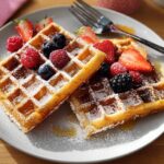 Two golden waffles topped with fresh strawberries, raspberries, blueberries, and powdered sugar, perfect for breakfast ideas recipes.