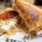 A perfectly grilled cheese sandwich, cut in half, with melted cheese oozing out, featuring caramelized onions.