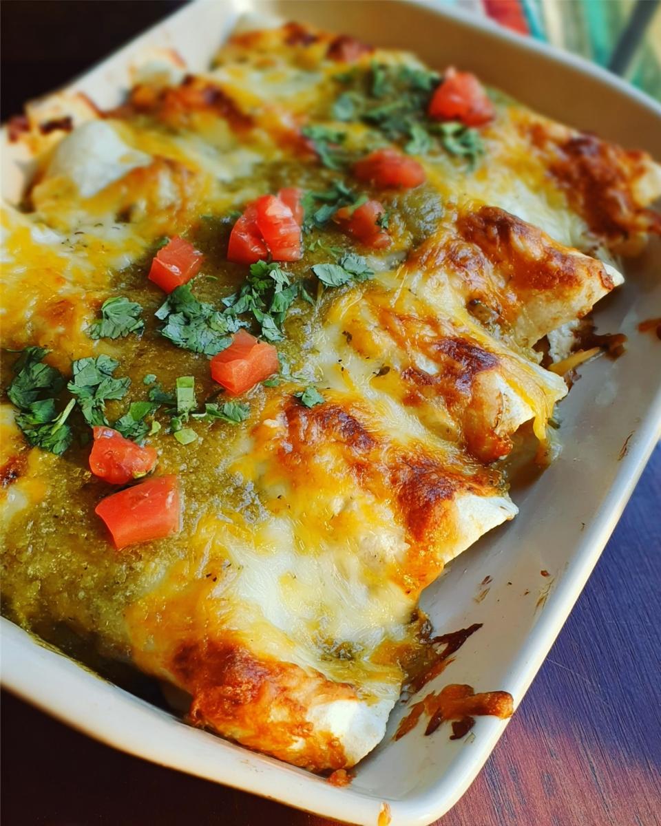 Close-up of baked chicken enchiladas topped with melted cheese, green sauce, diced tomatoes, and cilantro.
