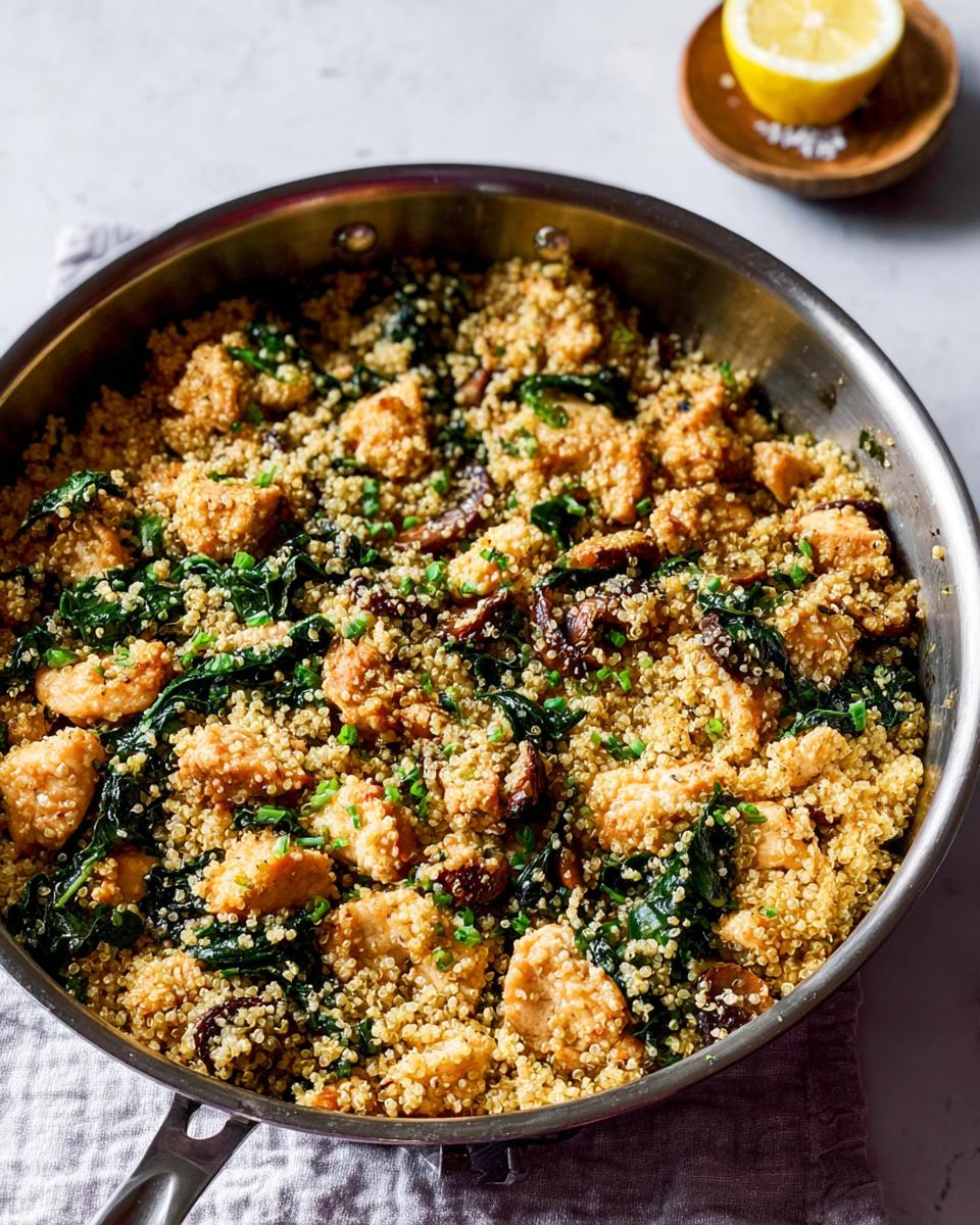 A close-up view of a skillet filled with a healthy chicken and quinoa dish, featuring tender chicken pieces, vibrant greens, and mushrooms.