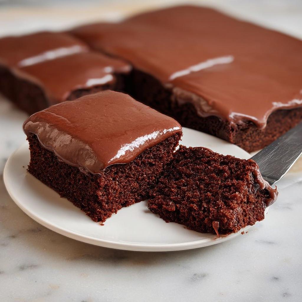 A slice of rich chocolate cake with smooth chocolate frosting, part of a larger cake.