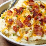 Close-up of creamy mashed potatoes recipe topped with melted cheese, crispy bacon bits, and fresh chives.