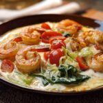 Close-up of a creamy shrimp recipe featuring plump shrimp, cherry tomatoes, and wilted spinach in a rich sauce.