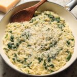 Close-up of creamy spinach orzo in a pan, topped with grated parmesan cheese and black pepper.