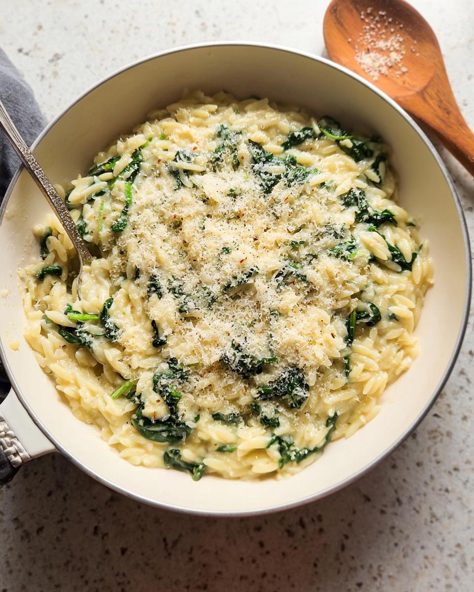 A close-up shot of creamy spinach orzo pasta, a delicious veggie side dish, topped with grated Parmesan cheese.