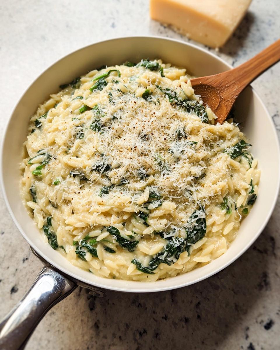 Creamy spinach orzo pasta dish in a white pan, topped with grated parmesan cheese. A perfect veggie sides recipe.