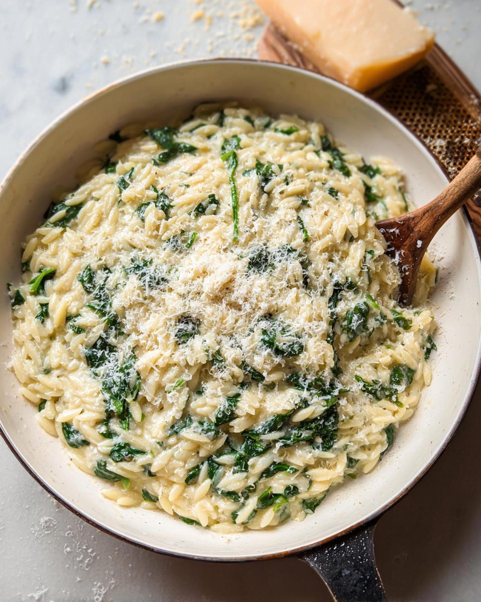 Close-up of creamy spinach orzo in a pan, topped with grated Parmesan cheese.