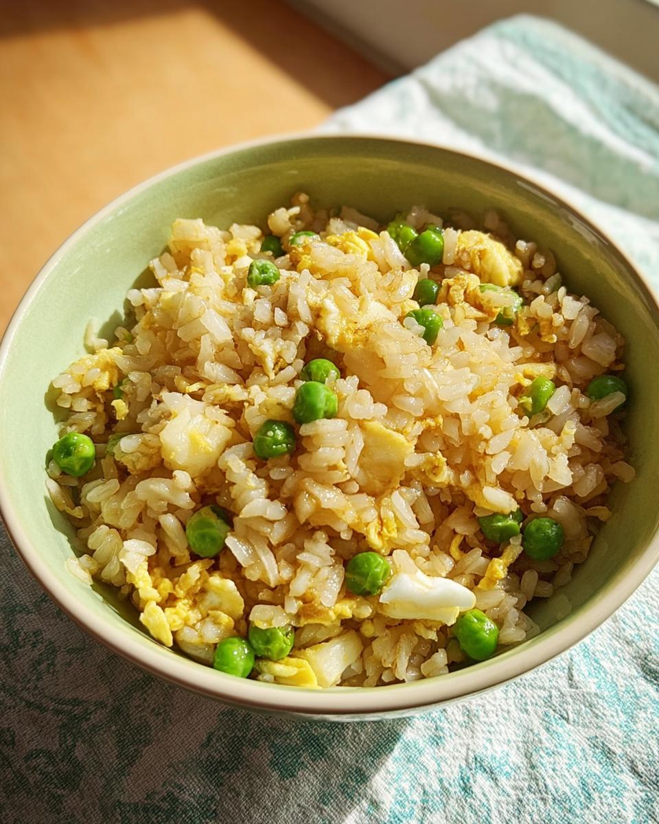 Close-up of a bowl of egg fried rice with peas, showcasing scrambled egg pieces and fluffy rice.