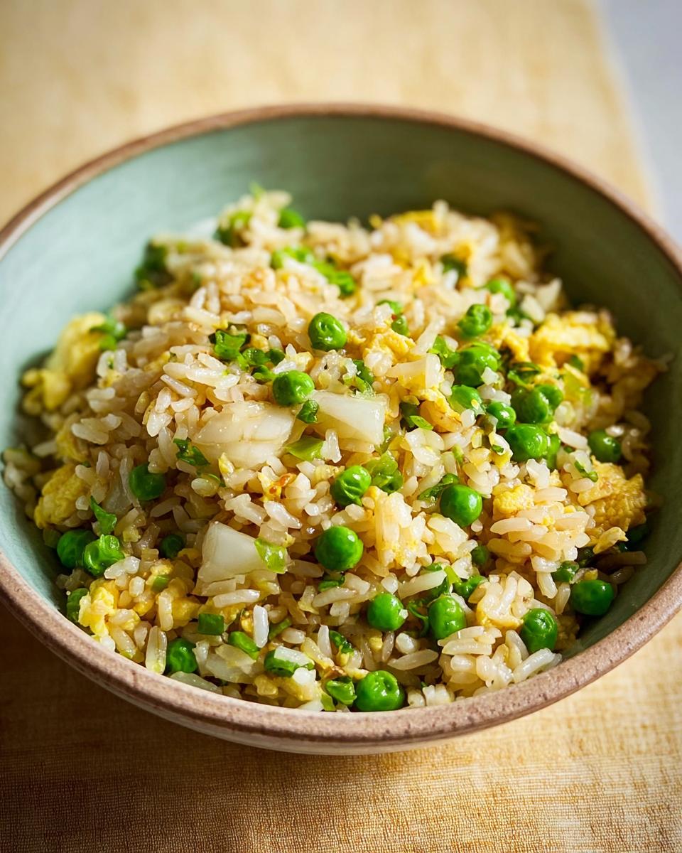A close-up of a bowl of egg fried rice with peas and chopped onions, part of 7-Ingredient Egg Recipes.