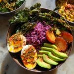 A vibrant bowl featuring two halves of a perfectly cooked egg, purple rice, sliced avocado, and roasted kale, showcasing one of the ultimate egg recipes for beginners.