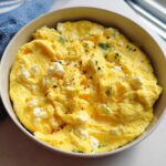 Close-up of a fluffy omelet in a bowl, topped with crumbled feta cheese, herbs, and red pepper flakes. The Only Egg Recipes.