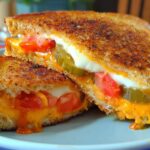 Close-up of a gooey grilled cheese sandwich cut in half, revealing melted cheese, tomato slices, and pickles.