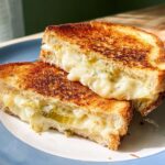 A close-up of a perfectly grilled cheese sandwich, cut in half, with melted cheese oozing out.