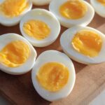 Several hard-boiled eggs, halved, revealing bright yellow yolks, arranged on a wooden board. Perfect for healthy meals recipes meal prep.