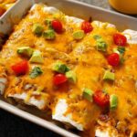 A baking dish filled with cheesy enchiladas topped with diced avocado, cherry tomatoes, and cilantro. Part of 25-Ingredient Healthy Meals Recipes.