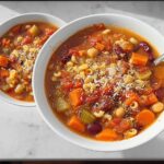 Two bowls of hearty vegetable soup recipe, filled with pasta, beans, carrots, and tomatoes, topped with grated cheese.