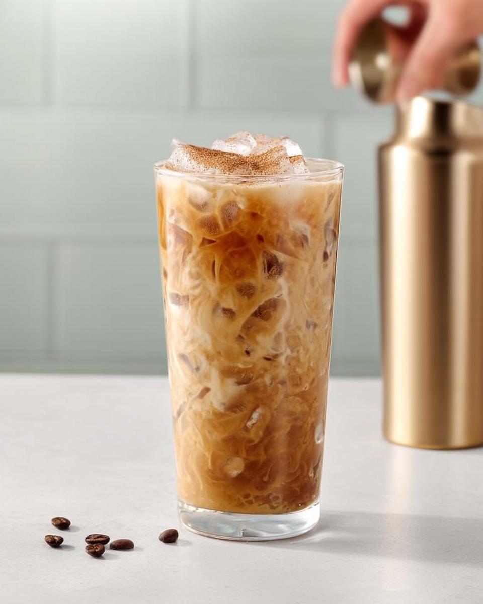 A tall glass of iced coffee with cream swirls, ice, and a sprinkle of cinnamon, part of Starbucks Drinks Recipes.