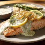 A beautifully plated salmon fillet with lemon slices, dill, and creamy sauce, served with rice and asparagus. One of 20 Genius Salmon Recipes.
