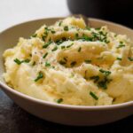 A bowl of fluffy mashed potatoes topped with fresh chives and black pepper, a perfect side dish.