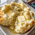 Close-up of a serving of creamy mashed potatoes recipe, topped with melting butter and herbs.
