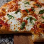 Close-up of a slice of pizza with melted cheese, tomato sauce, and fresh basil leaves, perfect for pizza night recipes.