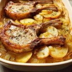 Two bone-in pork chops baked with sliced potatoes and onions in a casserole dish.