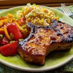 Two perfectly cooked pork chops with a glossy glaze, served with sautéed bell peppers and a corn salad.