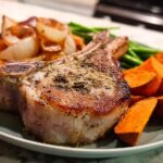 A perfectly cooked pork chop recipe served with roasted sweet potatoes, onions, and green beans.