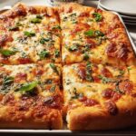 Close-up of a freshly baked rectangular pizza, cut into squares, topped with melted cheese and fresh basil for a quick pizza night recipe.