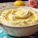 A close-up of creamy restaurant-style mashed potatoes served in a white bowl, topped with melted butter and black pepper.