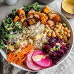 A vibrant and healthy rice bowl featuring brown rice, roasted sweet potatoes, chickpeas, kale, shredded carrots, red cabbage, and radish slices, drizzled with dressing.