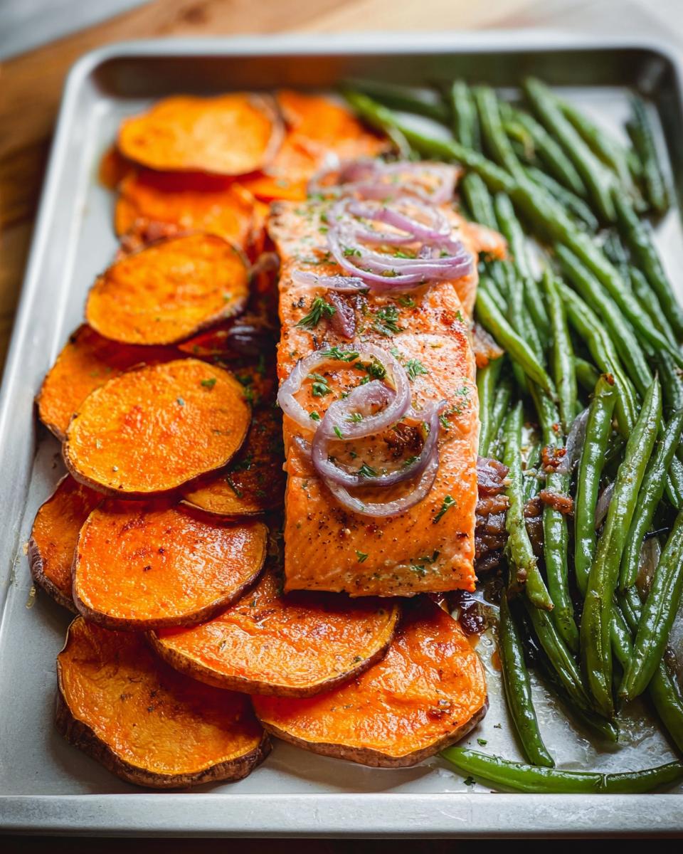 A delicious salmon fillet meal prep with roasted sweet potato slices and green beans on a baking sheet.