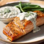 A perfectly cooked salmon fillet topped with creamy dill sauce and a side of green beans.