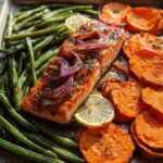 A perfectly cooked salmon fillet with roasted sweet potato slices and green beans on a baking sheet, ideal for salmon recipes meal prep.