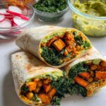 Two halves of a whole wheat wrap filled with roasted sweet potato, chickpeas, kale, and avocado.