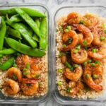Two glass containers filled with shrimp recipes meal prep: one with brown rice, shrimp, and green onions, the other with brown rice, shrimp, and snap peas.