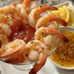 Close-up of a classic shrimp cocktail appetizer with perfectly cooked shrimp, cocktail sauce, and lemon wedges.