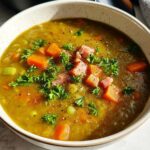 A close-up of a bowl of hearty split pea soup recipe with ham, carrots, and parsley.