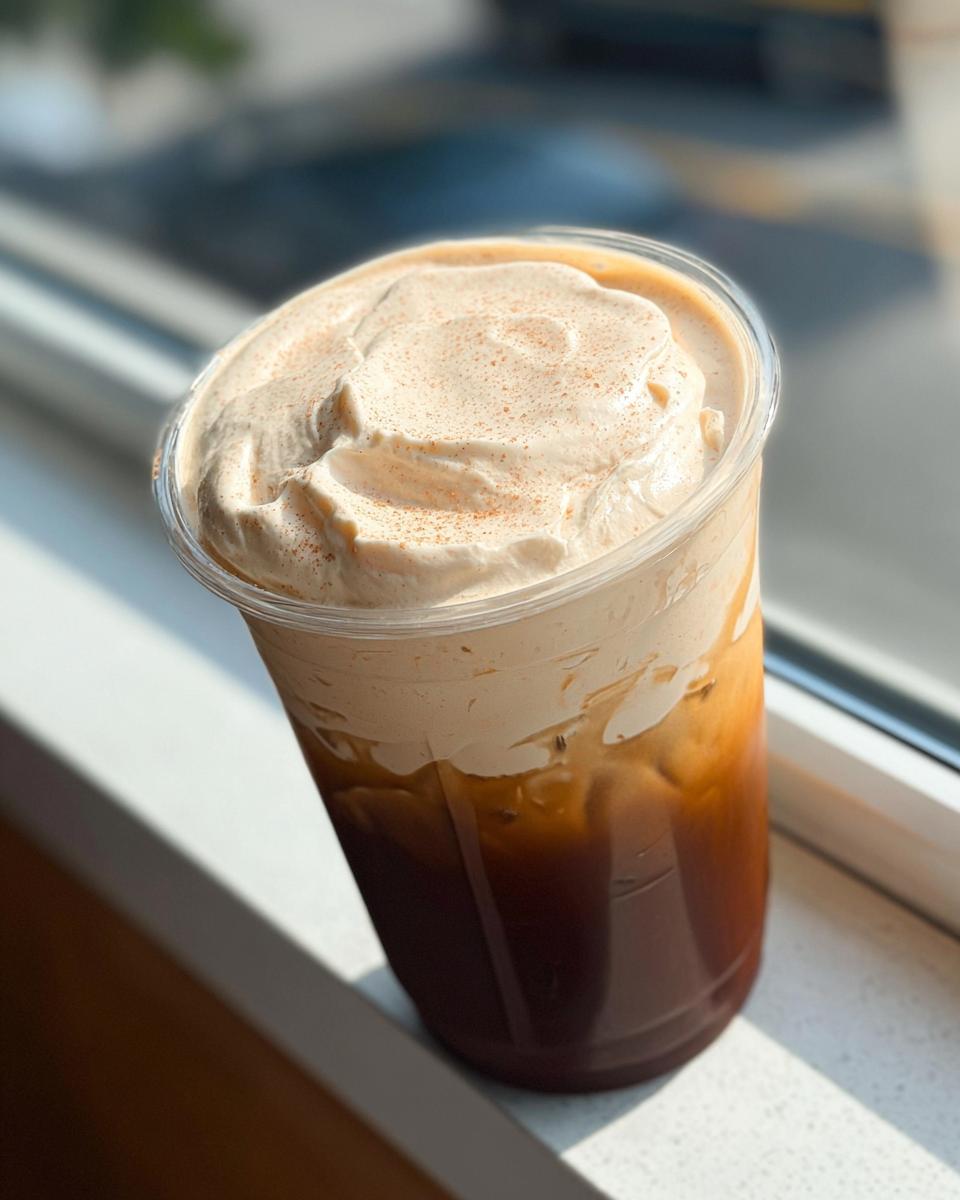 A tall iced coffee drink with a generous swirl of whipped cream and a sprinkle of cinnamon, perfect for a Restaurant-Style Starbucks Drink Recipe.