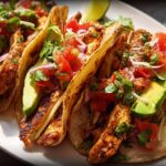 A close-up of several delicious chicken tacos filled with seasoned chicken, avocado, tomato, onion, and cilantro, perfect for Taco Tuesday Recipes Meal Prep.