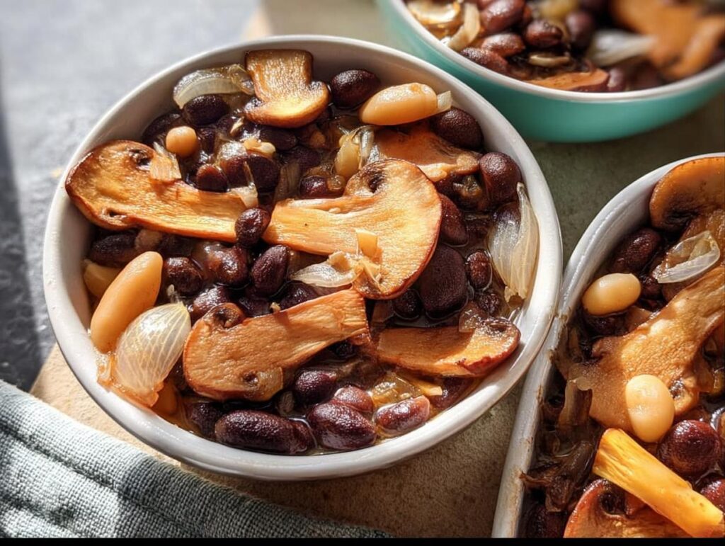 Close-up of a bowl filled with a hearty veggie sides recipe featuring dark beans, sliced mushrooms, and onions.
