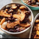 Close-up of a bowl filled with a hearty veggie sides recipe featuring dark beans, sliced mushrooms, and onions.
