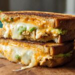 A delicious Chicken Avocado Melt Sandwich stacked, with melted cheese oozing out.